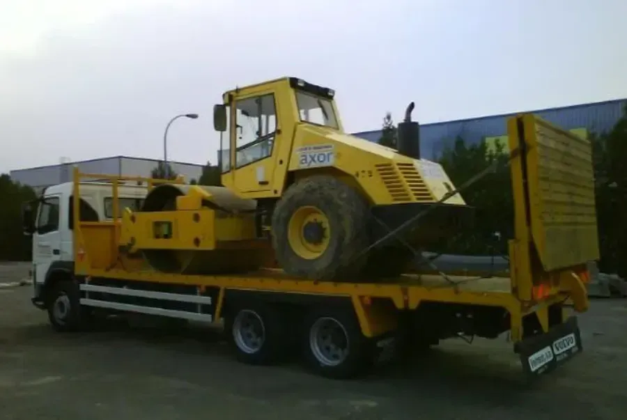 Una cargadora de construcción amarilla montada sobre un camión de plataforma está estacionada al aire libre en un lote.