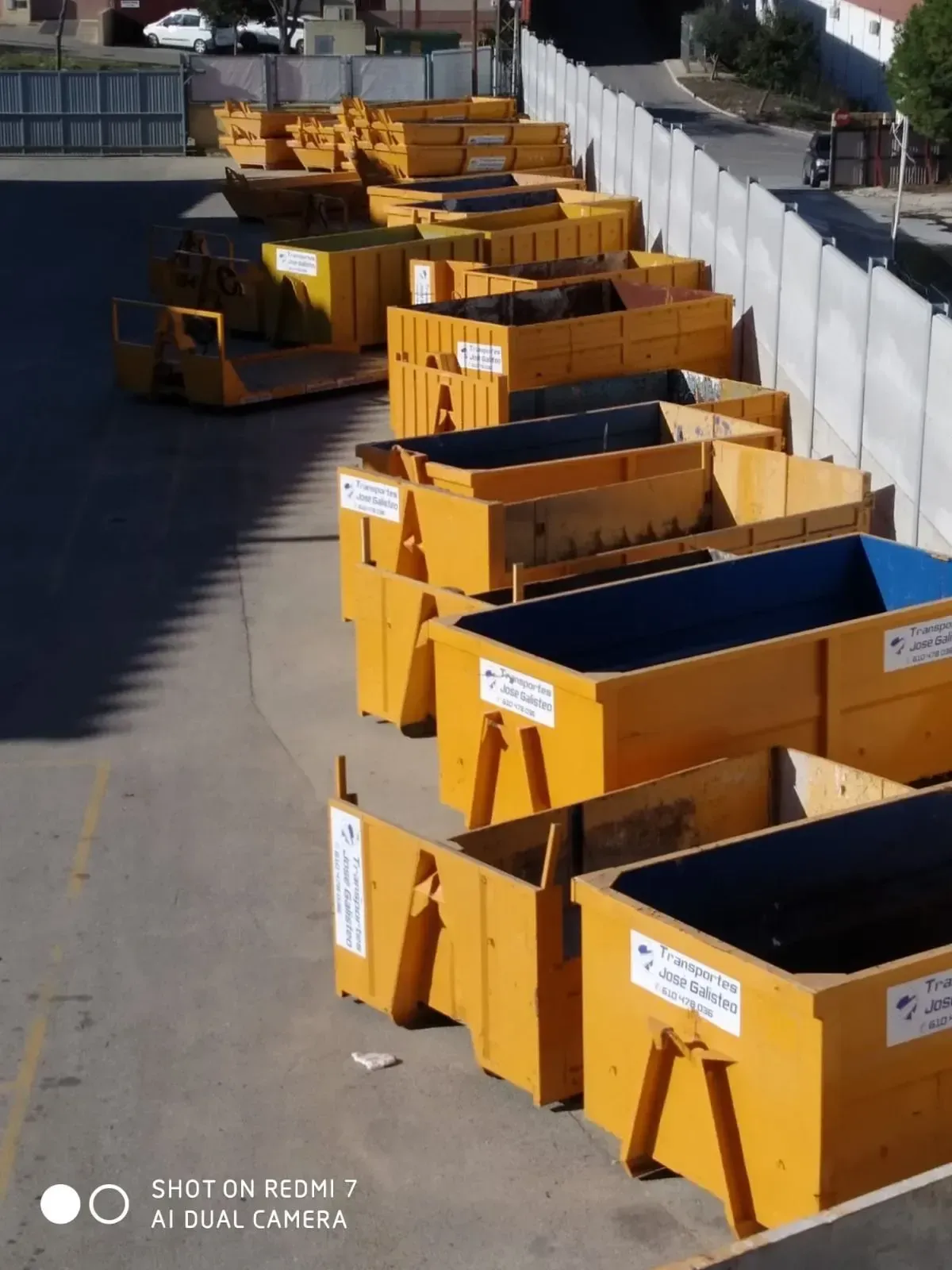 Una hilera de grandes contenedores industriales amarillos se alineaba a lo largo de una calle pavimentada