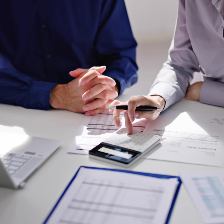 Manos sobre la mesa con papeleo y calculadora. Alguien está calculando.