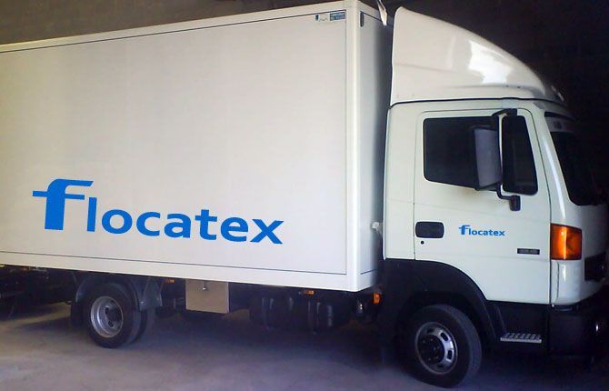 Camión de reparto Flocatex de color blanco estacionado en el interior, con logotipo azul en el lateral.