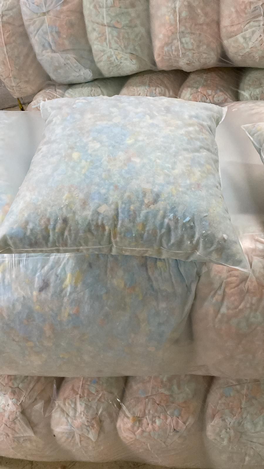 Pila de bolsas de plástico transparente llenas de material triturado de color azul y rosa.