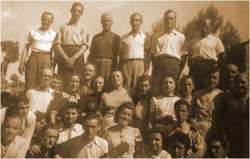 Foto grupal de hombres y mujeres al aire libre, en tono sepia. Personas en diversas poses, algunas sonriendo.