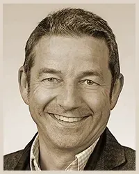 Auf einem Schwarzweißfoto lächelt ein Mann mit Bart und Brille.