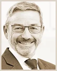 Auf einem Schwarzweißfoto lächelt ein Mann mit Bart und Brille.