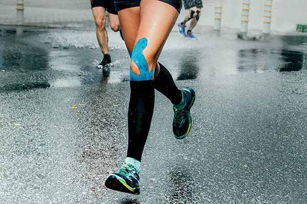 Eine Person mit Kinesio-Tape am Bein läuft im Regen.