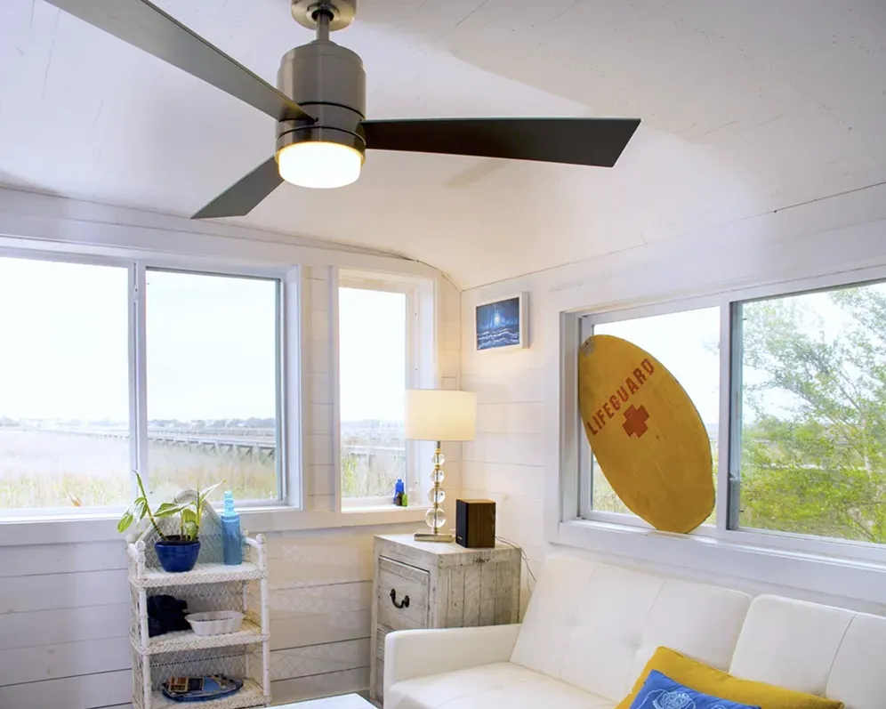 A room with a ceiling fan and a surfboard that says lifeguard on it