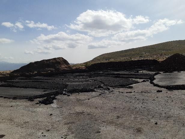 Un campo de tierra con una montaña al fondo y un cielo azul con nubes.