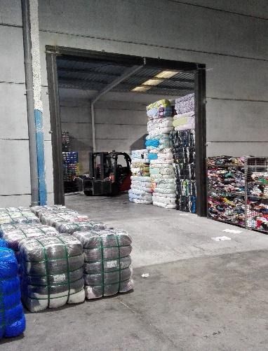 Un almacén lleno de muchas bolsas de ropa y una carretilla elevadora.