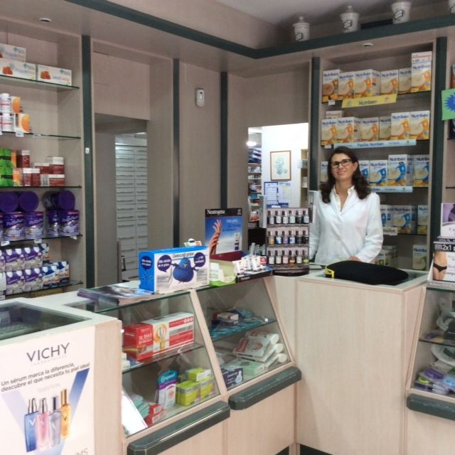 Un farmacéutico se encuentra detrás del mostrador de una farmacia, rodeado de estantes con medicamentos y productos de salud.
