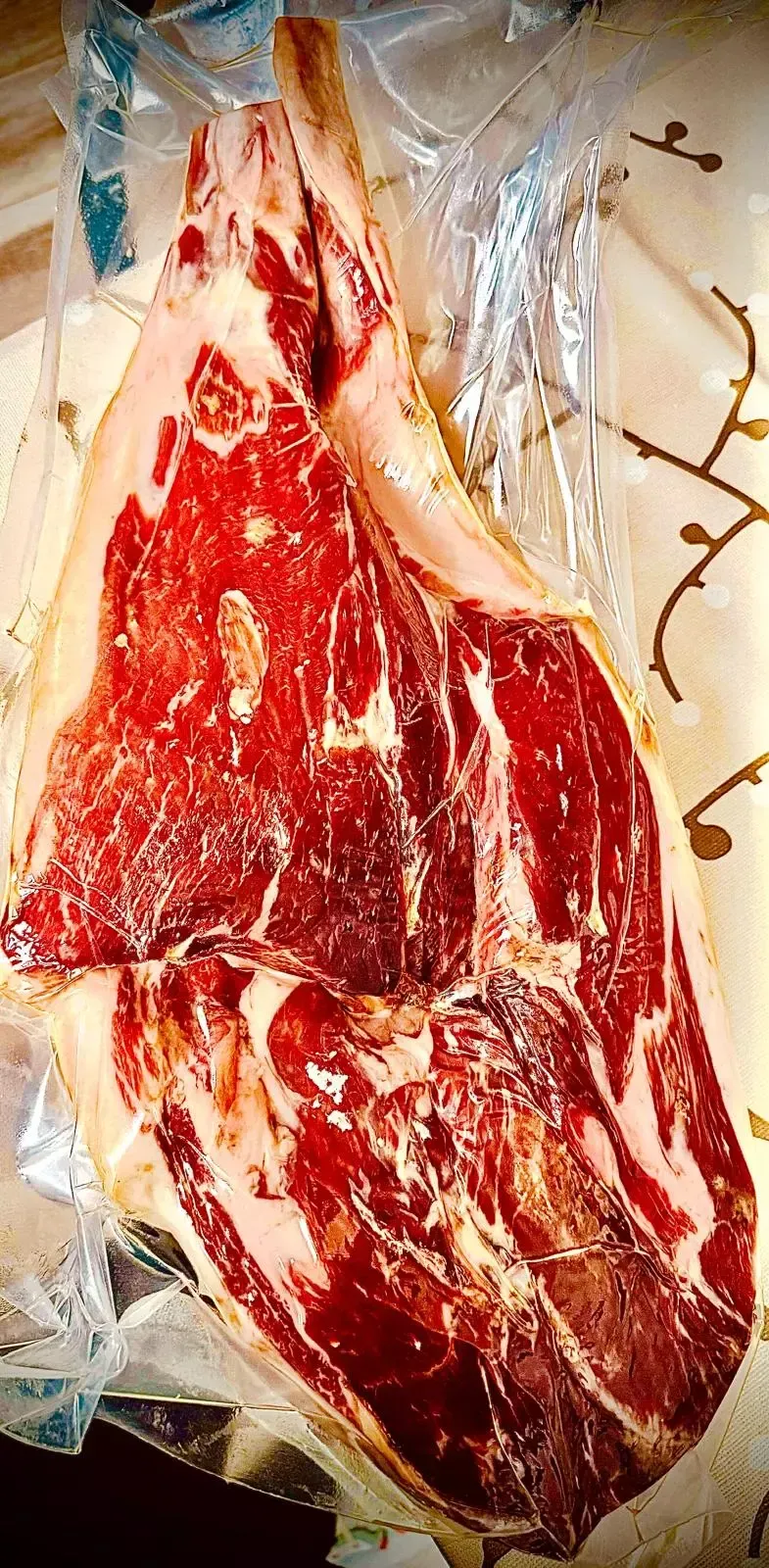 Filete de tomahawk crudo envuelto en plástico, listo para preparar. La carne es de un rojo vibrante con vetas blancas.