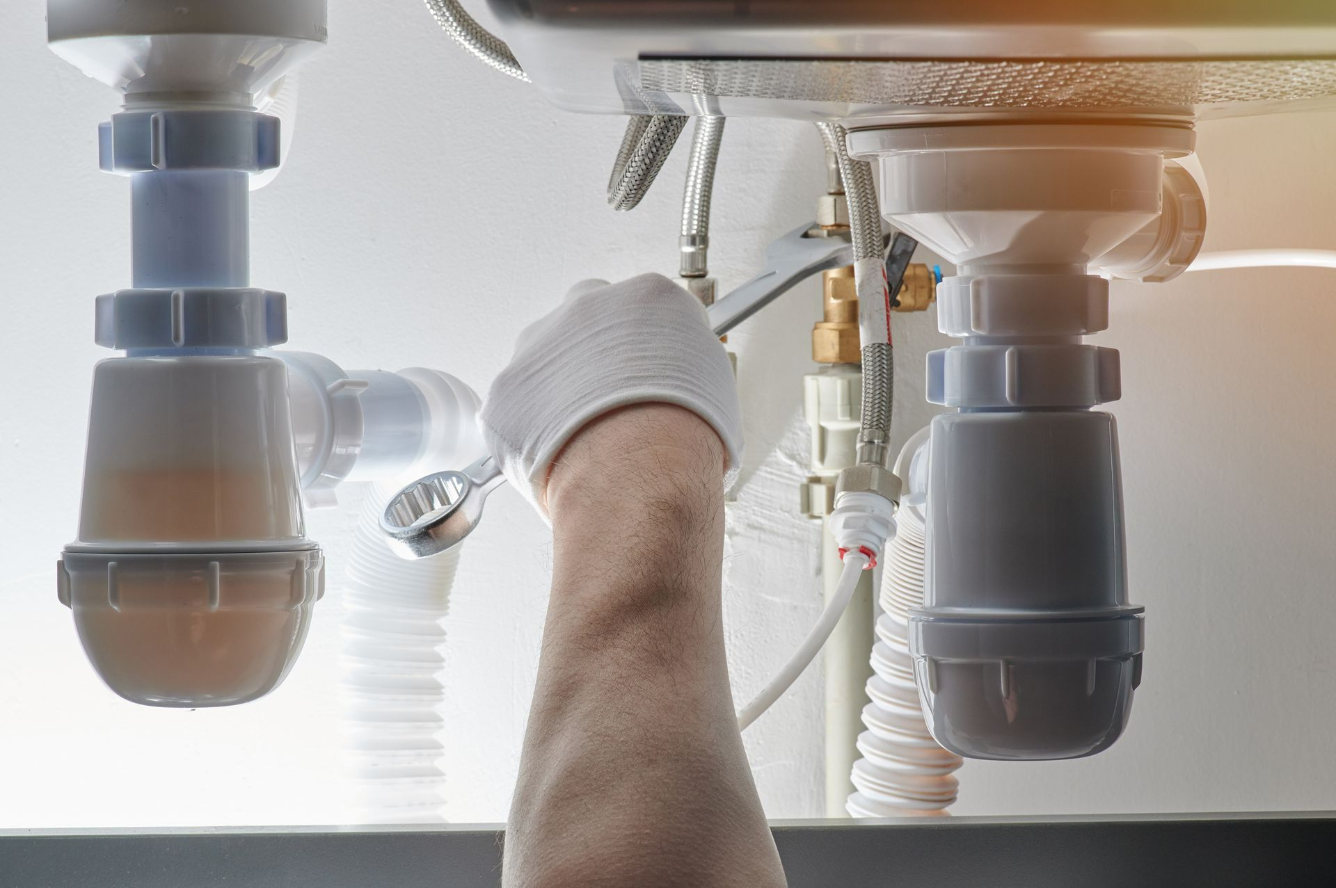 Main d'un plombier tenant une clé plate et travaillant sous un évier