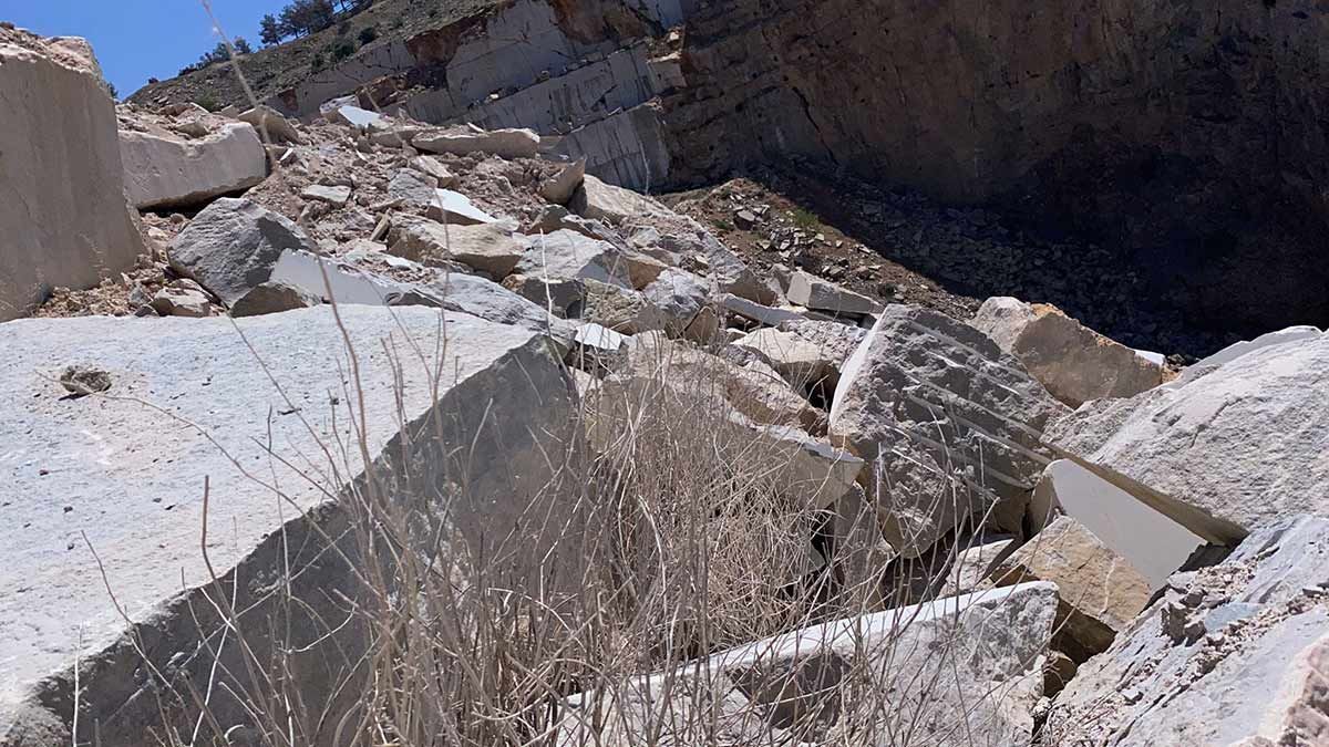 Campo de escombros de bloques de hormigón rotos; maleza seca en primer plano, ladera en el fondo.