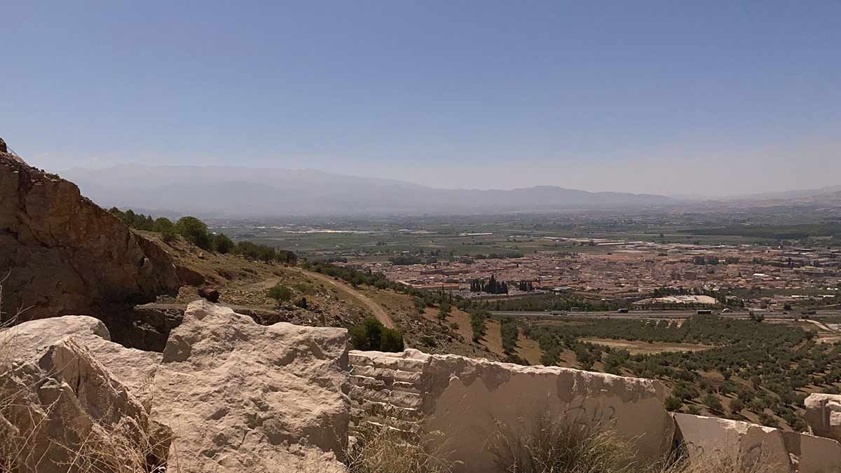 Vista de una ciudad desde un mirador sobre una ladera rocosa bajo un cielo azul brillante.