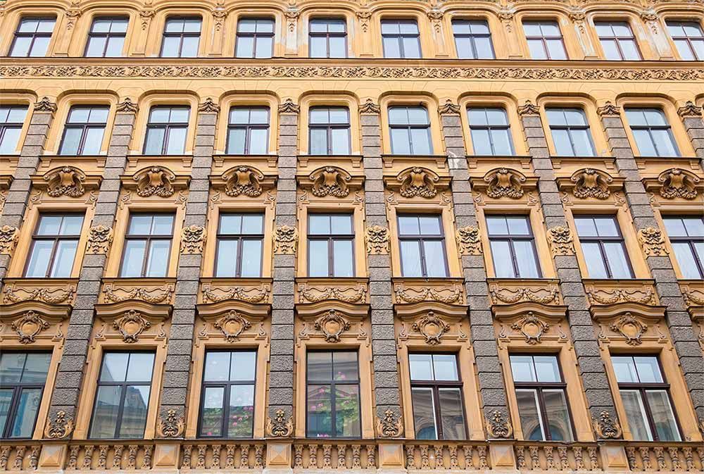Fachada de edificio adornada de color amarillo y marrón con numerosas ventanas.