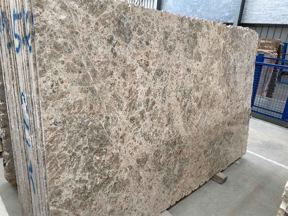 Pila de grandes losas de mármol beige con vetas marrones.