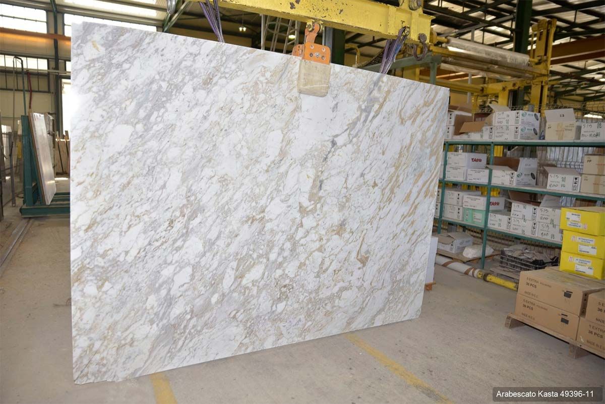 Una gran losa de granito blanco y dorado siendo levantada por una grúa en un almacén.