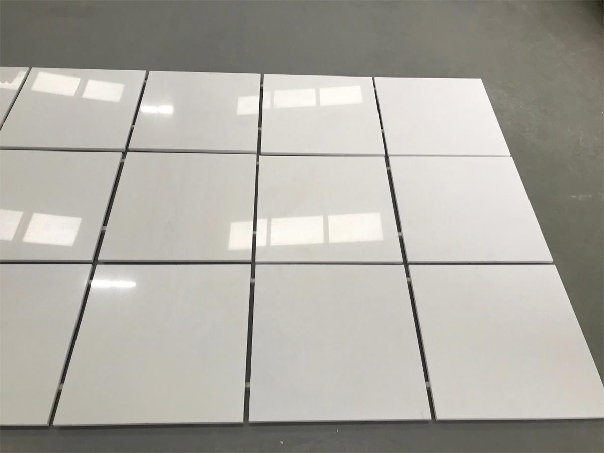 Azulejos blancos dispuestos en un patrón de cuadrícula, con líneas de lechada oscuras, sobre una superficie gris.
