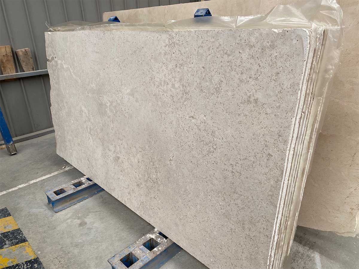 Grandes losas de piedra de color claro apiladas en un almacén, posiblemente para encimeras.
