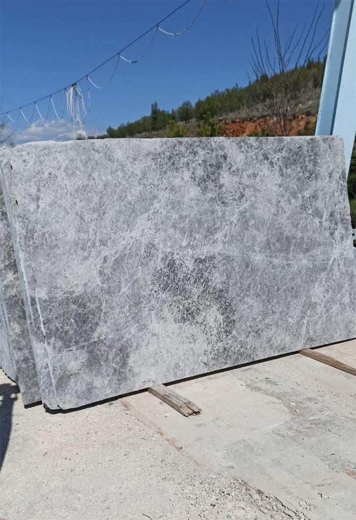 Losas de piedra gris apiladas al aire libre contra un cielo azul, sobre una superficie de hormigón.