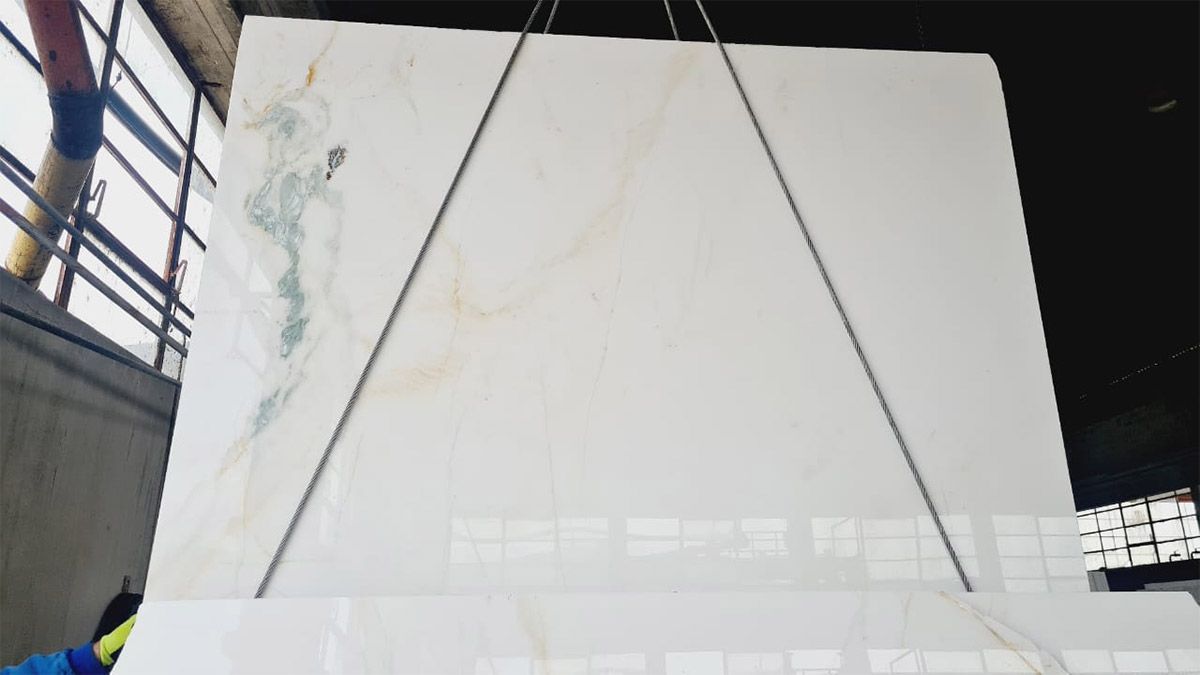 Gran losa de mármol blanco que se levanta, mostrando vetas verdes y doradas.