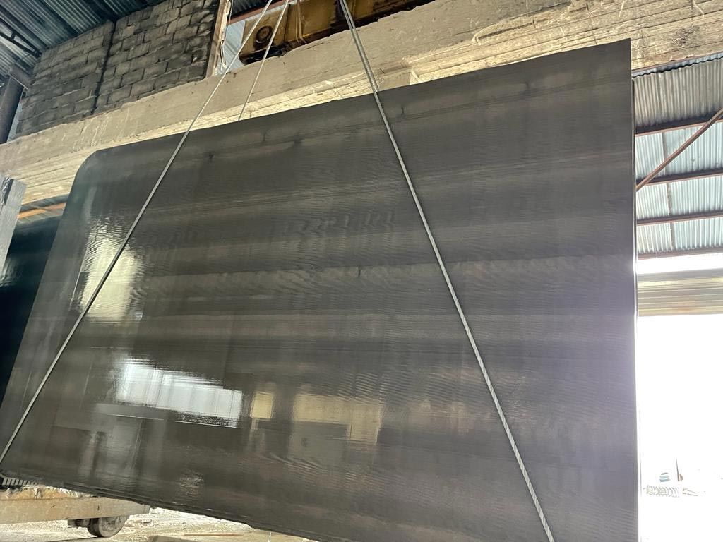 Gran losa rectangular de piedra oscura suspendida por cables en un entorno de almacén.