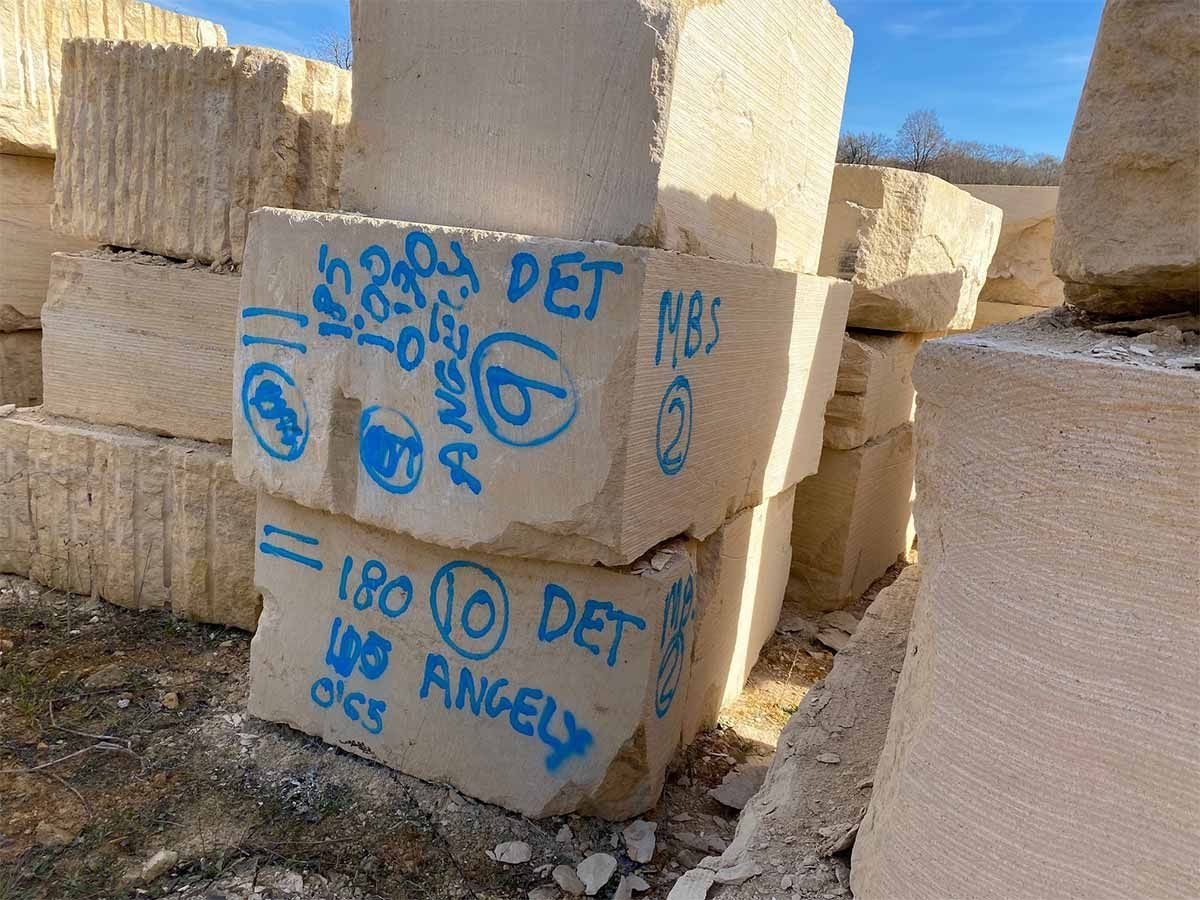 Bloques de piedra apilados al aire libre, marcados con texto azul que incluye