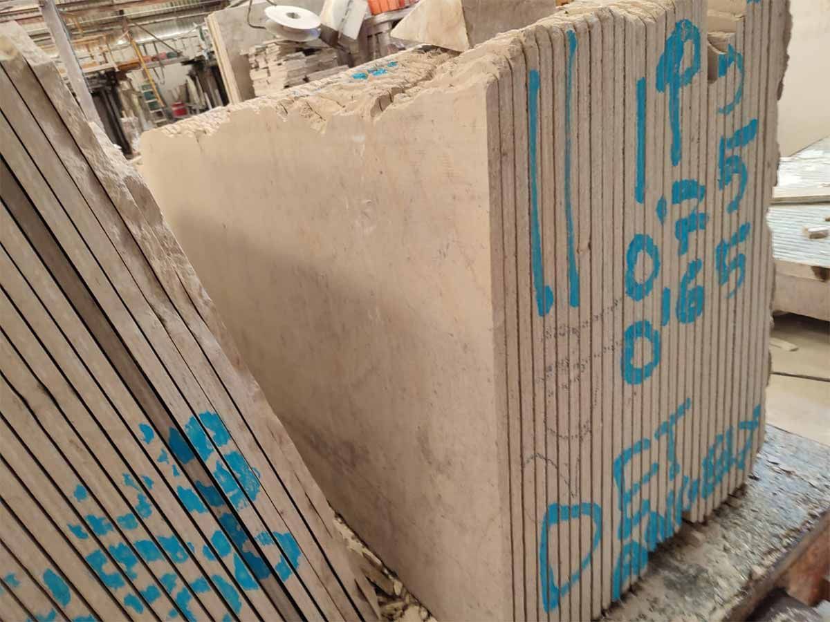 Bloques de piedra beige con marcas azules. Cantos aserrados visibles. Entorno industrial.