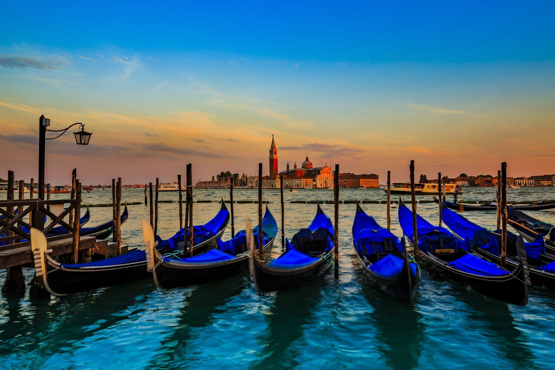 A row of blue gondolas are docked in the water.