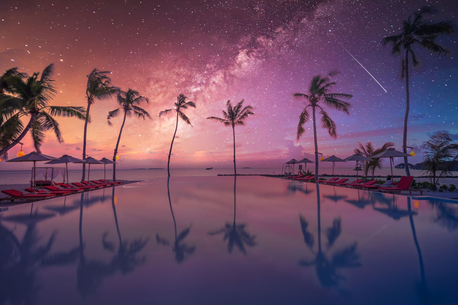 A swimming pool surrounded by palm trees under a starry sky at sunset.
