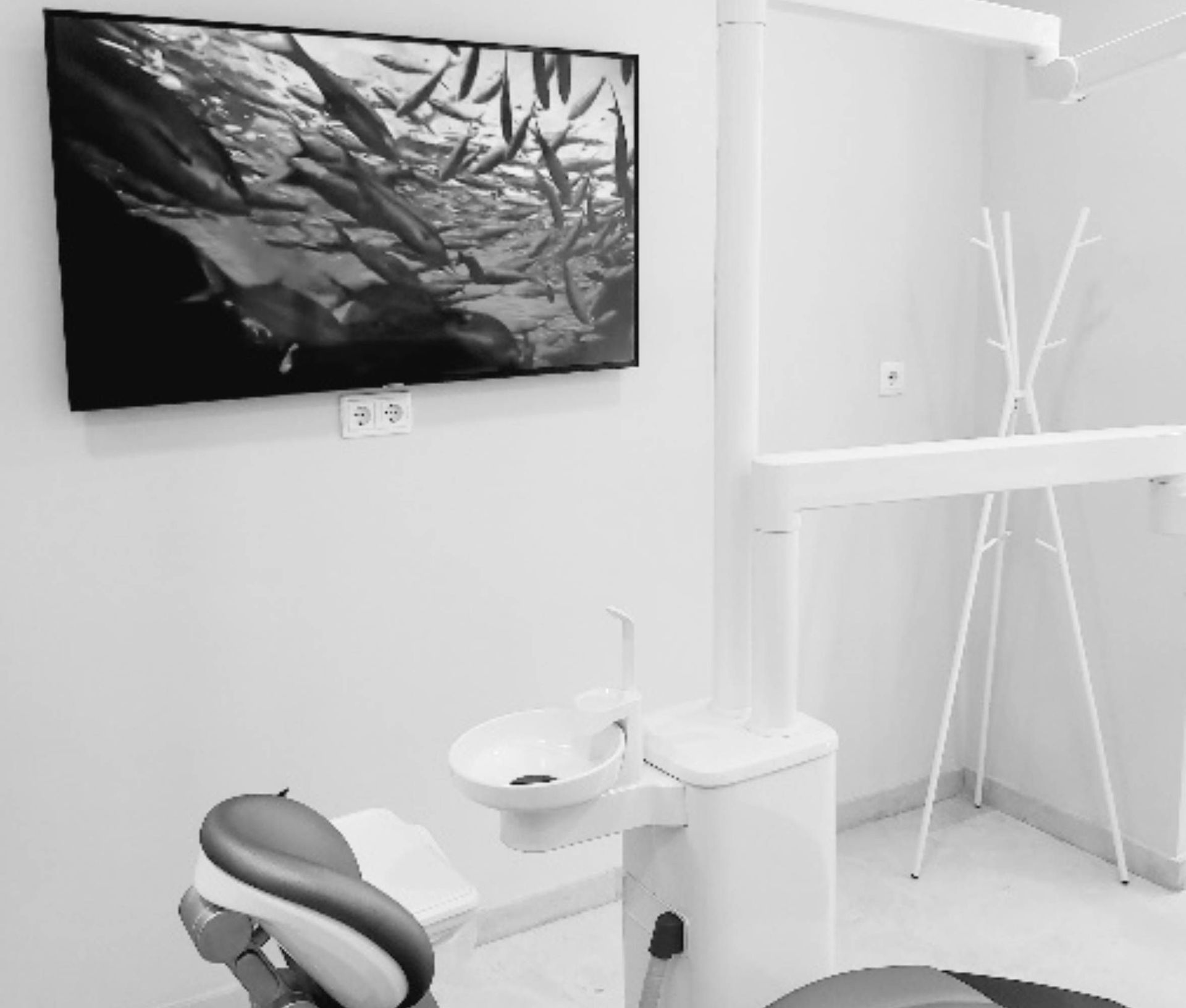 Interior de consultorio dental en blanco y negro con un televisor montado que muestra peces y equipos dentales.