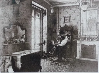Interior de una habitación en tonos sepia. Una persona está sentada en una silla junto a una ventana. También se ven un lavabo y una chimenea.