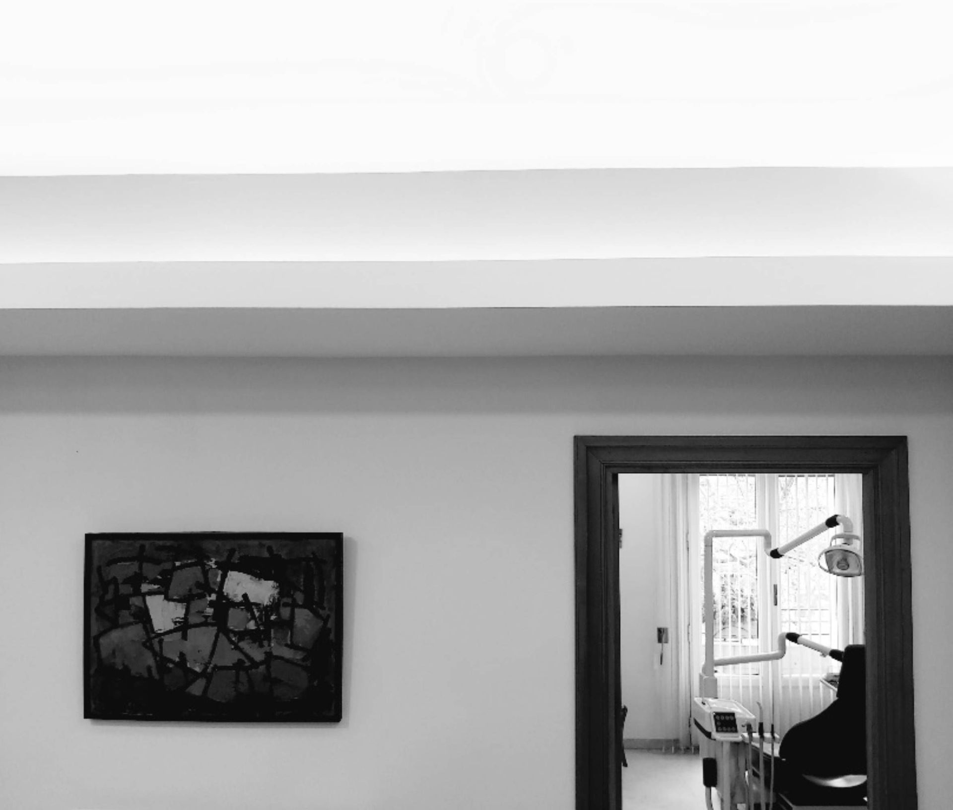 Vista en blanco y negro de un consultorio dental, que muestra obras de arte en la pared, la puerta y el equipo dental.