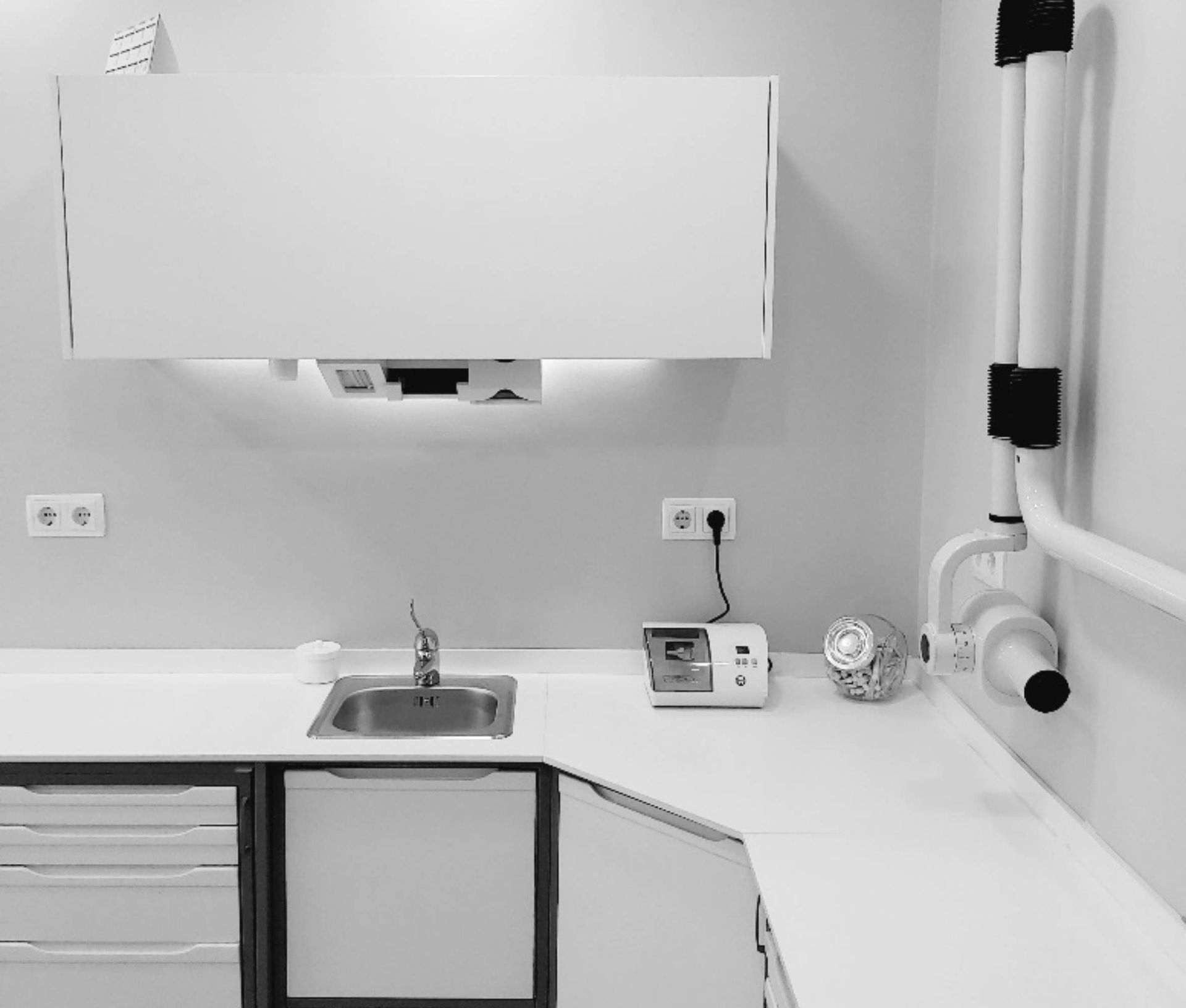 Rincón de consultorio dental blanco con lavabo, armarios y equipo de rayos X.