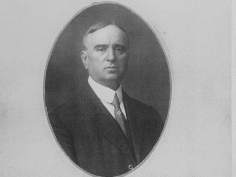 Retrato de un hombre de aspecto serio con traje, dentro de un marco ovalado.