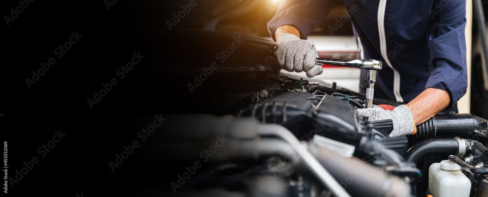 Un meccanico con i guanti lavora al motore di un'auto con una chiave inglese.