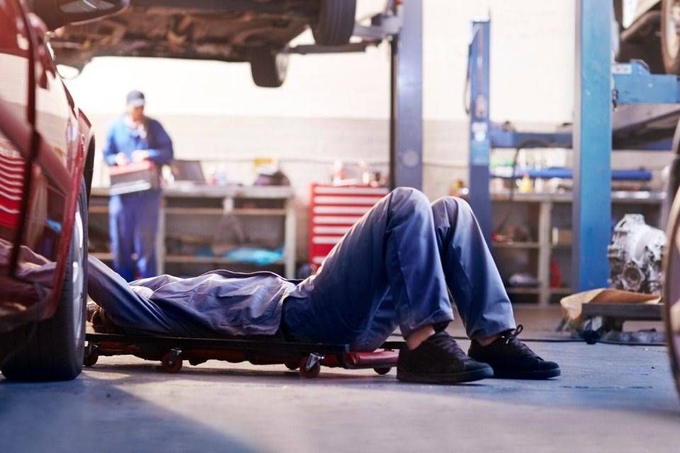 In un'officina meccanica, un meccanico lavora sotto un'auto su un carrello da officina.