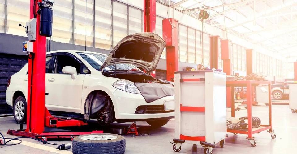 In un'officina, un meccanico è sdraiato su un carrello sotto un'auto sollevata.