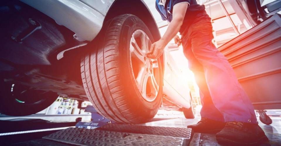 Un tecnico sdraiato su un carrello da meccanico sotto un veicolo in un'officina, intento a utilizzare un attrezzo.