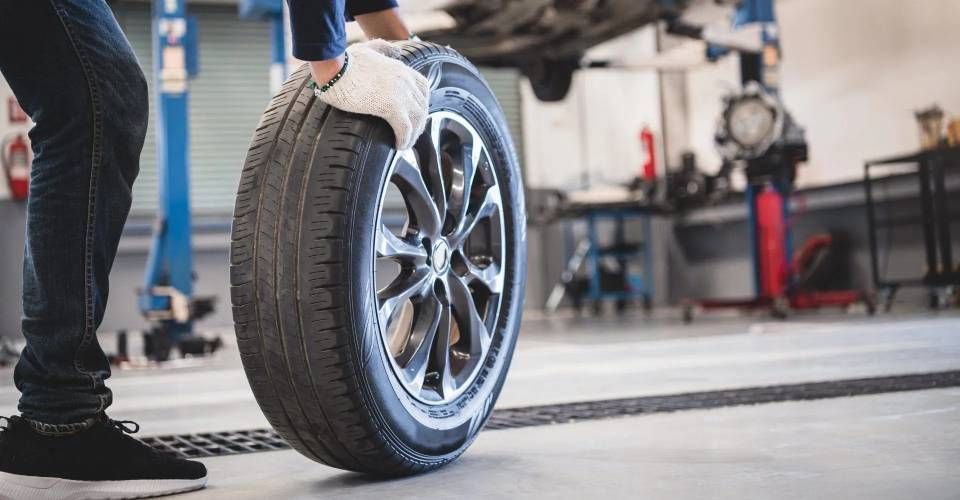Un meccanico con i guanti sposta uno pneumatico e un cerchione sul pavimento di un'officina meccanica.