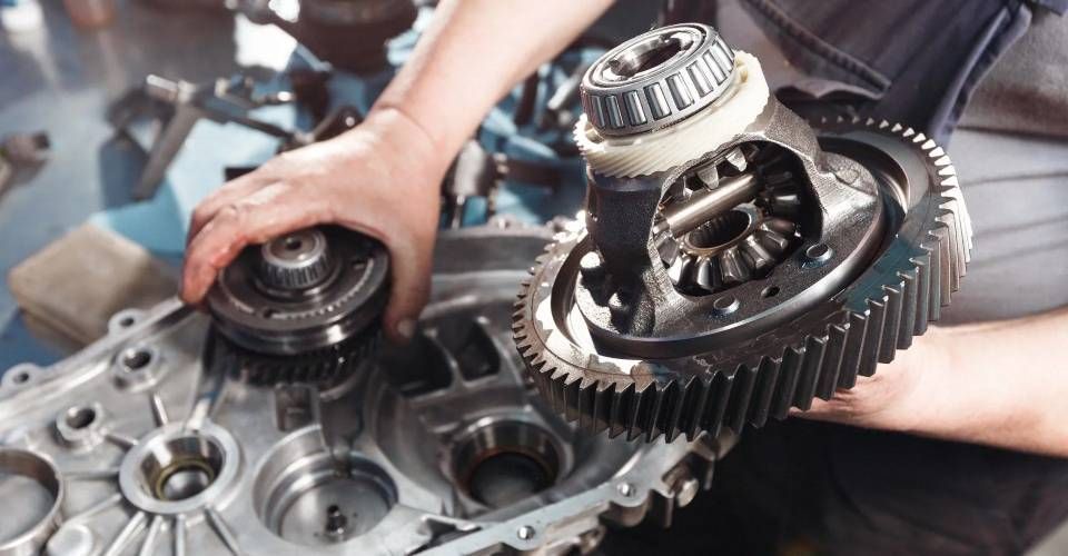 Un meccanico in tuta blu scuro tiene in mano due chiavi inglesi, in piedi davanti a un'auto bianca.