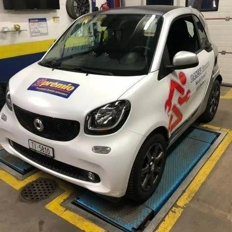Una Smart bianca parcheggiata su un ponte sollevatore all'interno di un'officina.