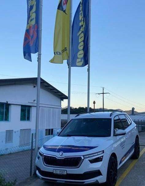 Un'auto Skoda bianca parcheggiata davanti a un edificio con bandiere Goodyear che sventolavano sopra.