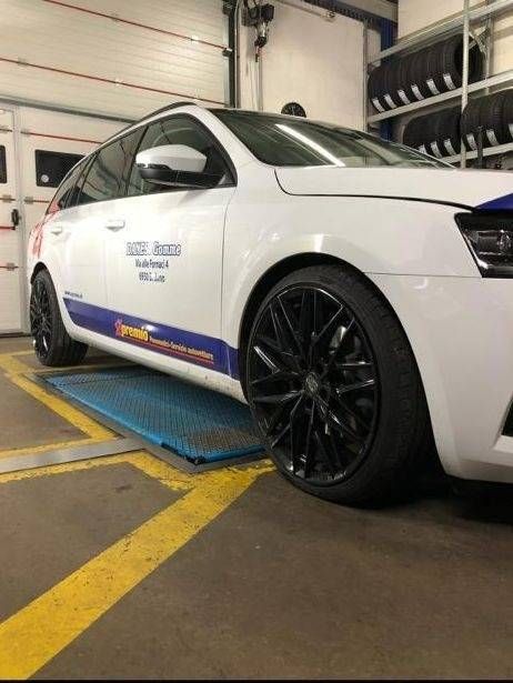 Una station wagon bianca con cerchi neri parcheggiata su un ponte sollevatore blu all'interno di un garage.