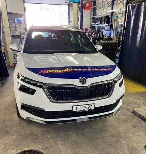 Una Škoda Karoq bianca parcheggiata all'interno di un'officina meccanica con uno striscione blu e giallo.