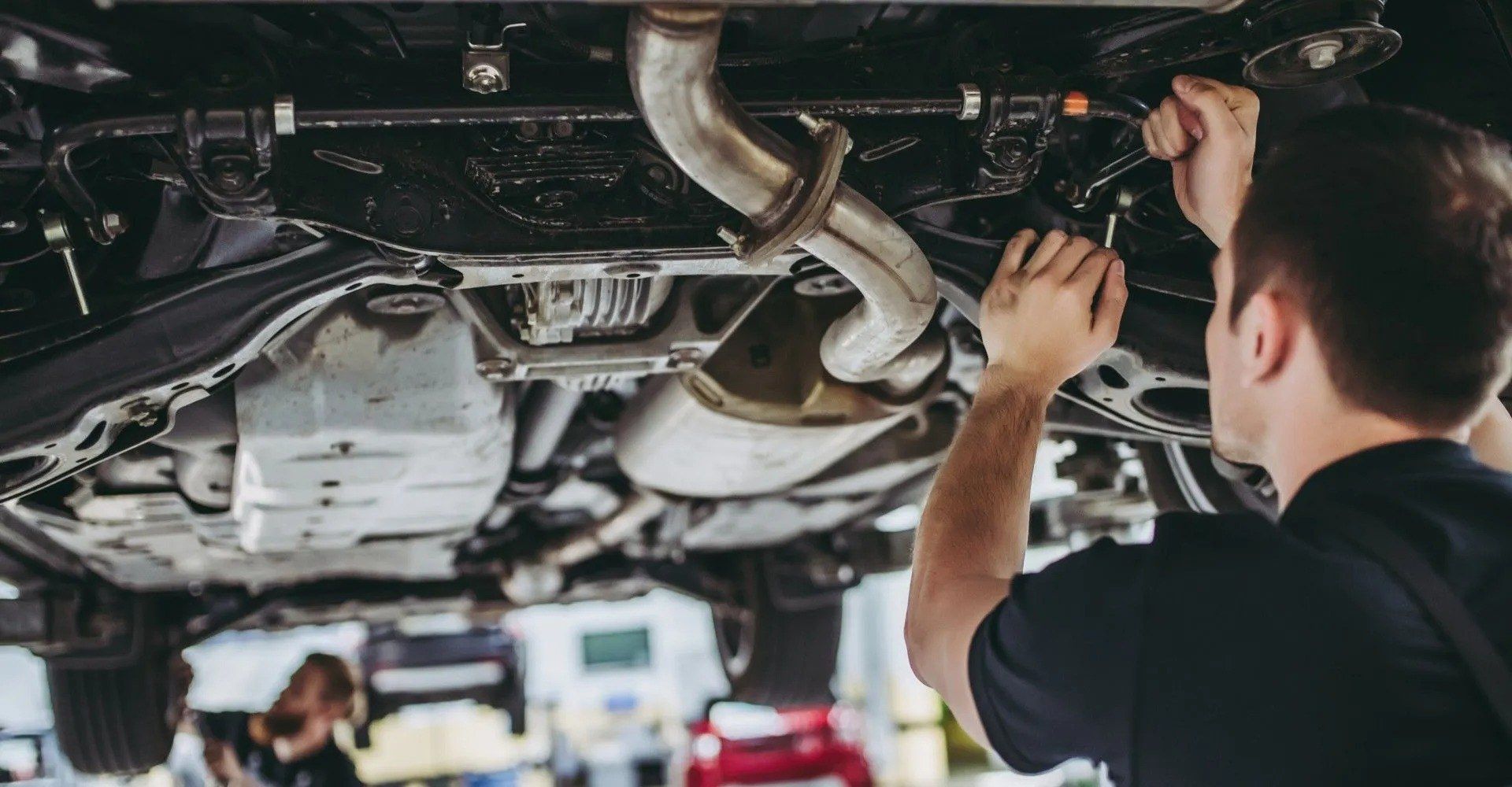 In un'officina meccanica, un tecnico con i guanti lavora sul passaruota posteriore di un veicolo scuro.