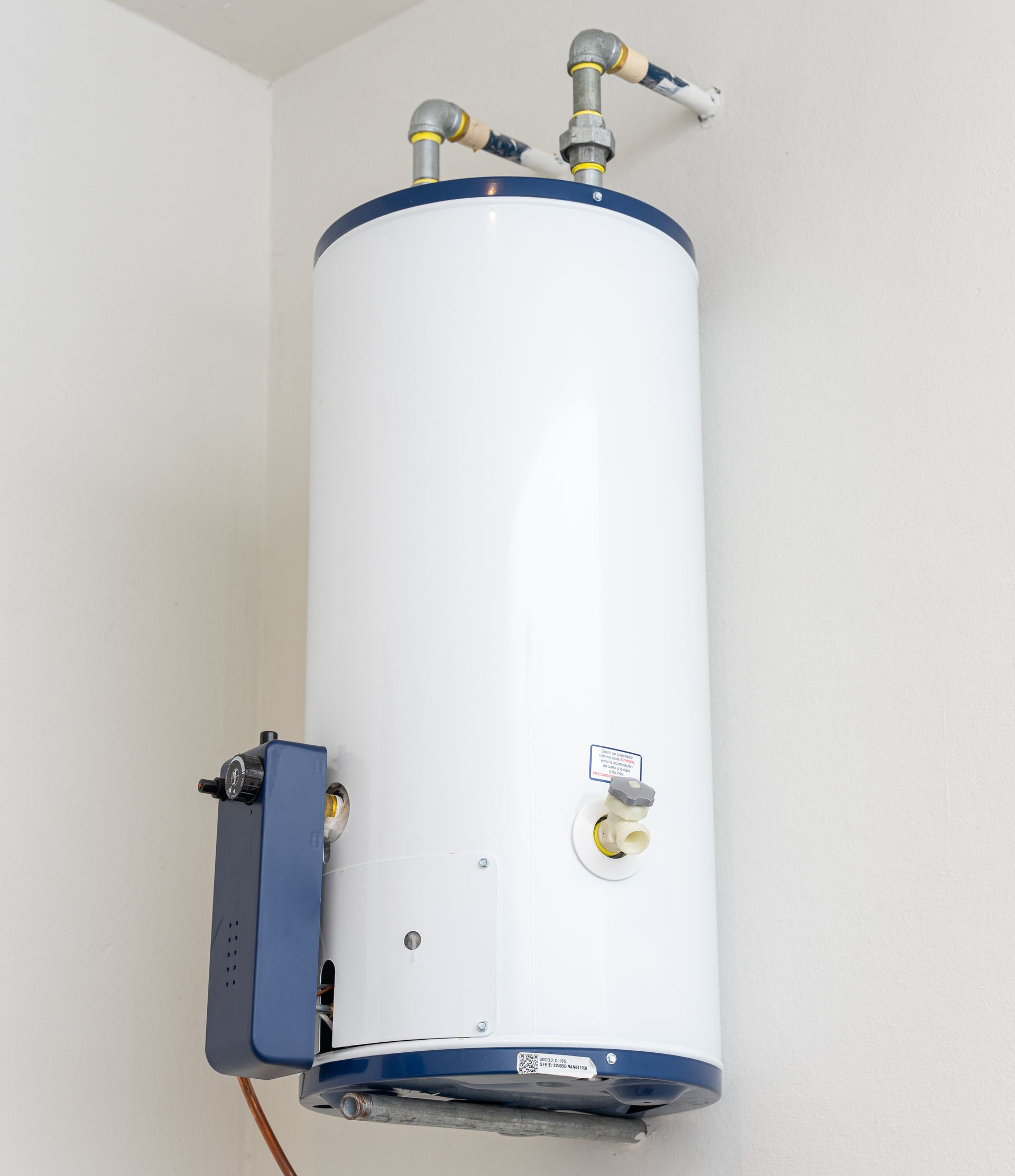 Chauffe-eau blanc contre un mur blanc avec des touches de bleu et des tuyaux raccordés.