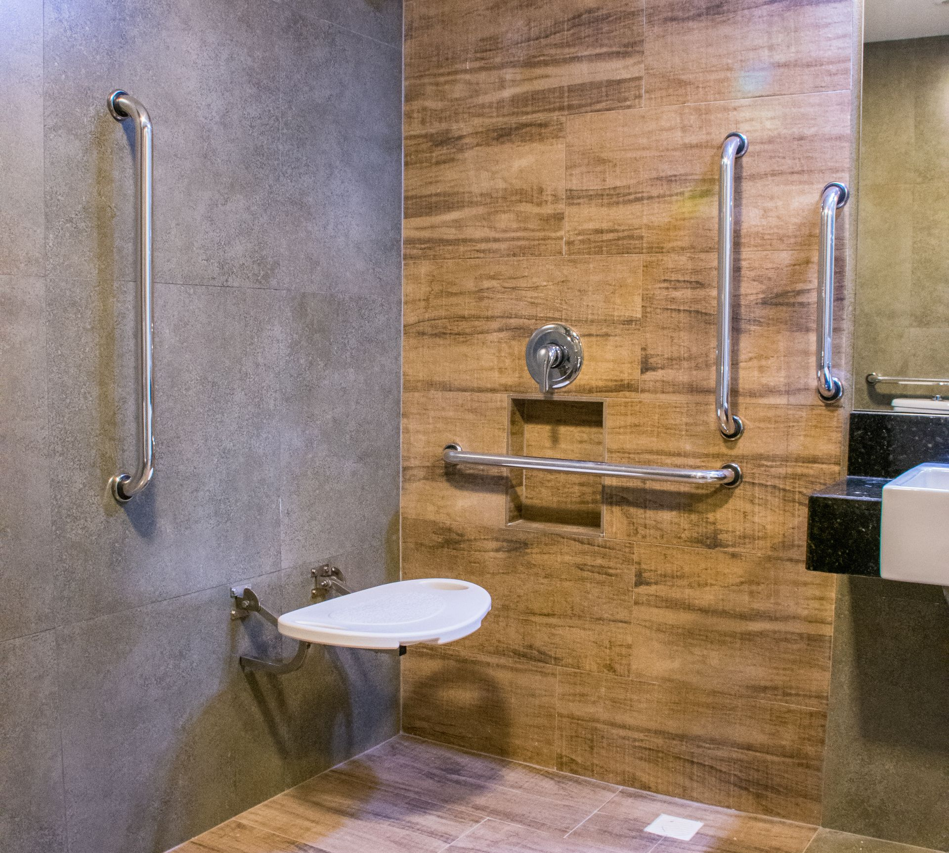 Salle de bains accessible avec barres d'appui, siège de douche et murs carrelés.