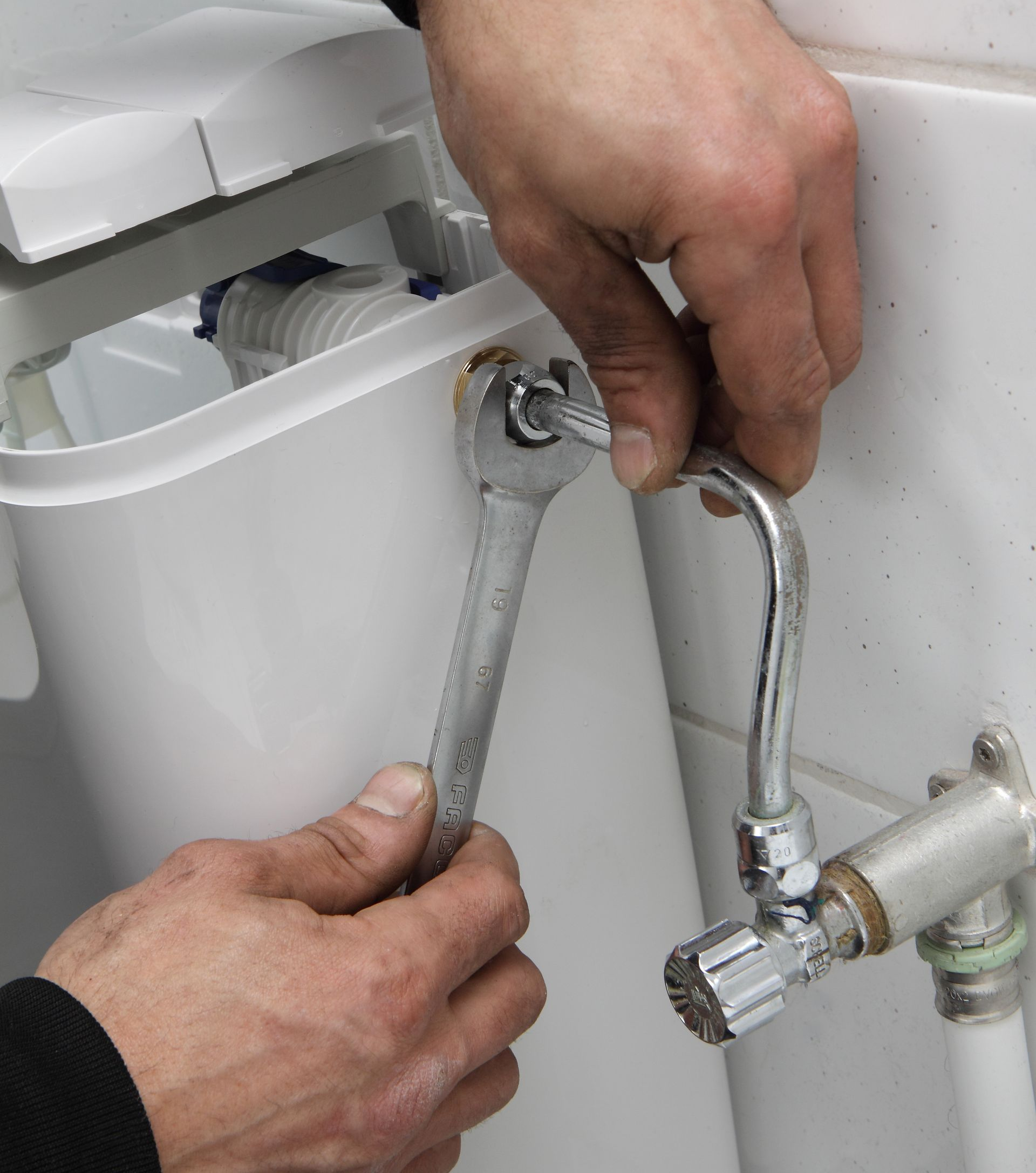 Une personne utilise une clé pour serrer un raccord de tuyau près d'un réservoir de toilettes blanc.