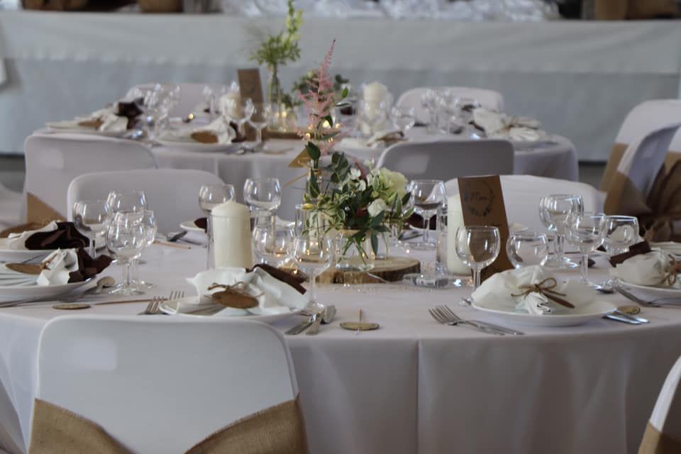 Tables de banquet dressées avec des nappes blanches, de la vaisselle, des bougies et centres de table floraux.
