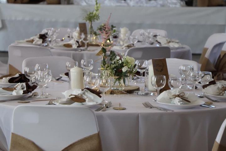 Tables de banquet dressées avec des nappes blanches, de la vaisselle, des bougies et centres de table floraux.